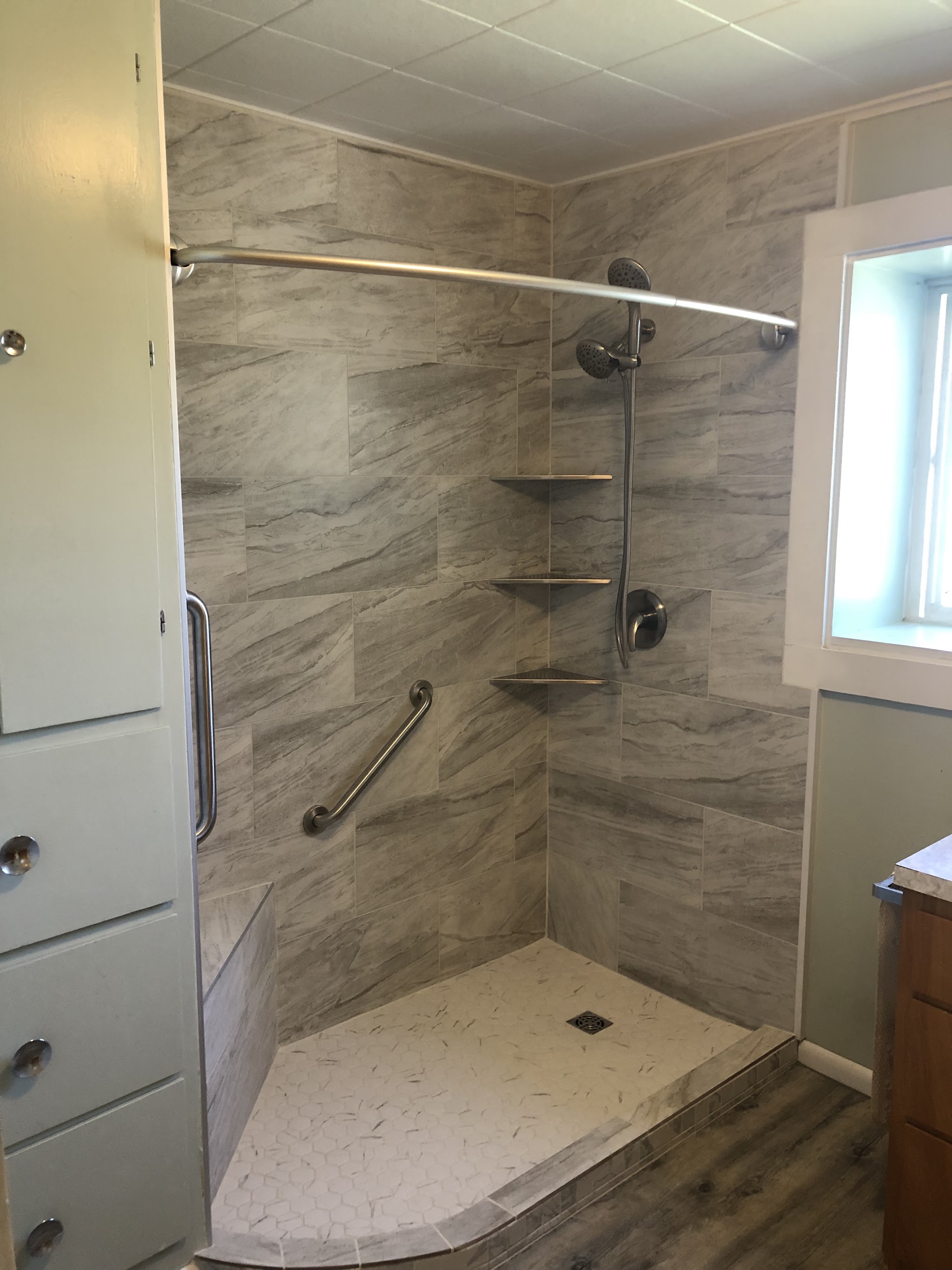 Finished walk-in shower with marble look tile, grab bar, corner shelves and a low threshold