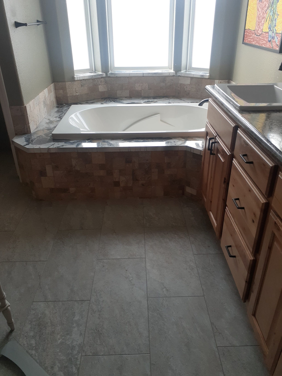 Bathroom with a drop-in soaking tub, travertine surround and large format tile floor