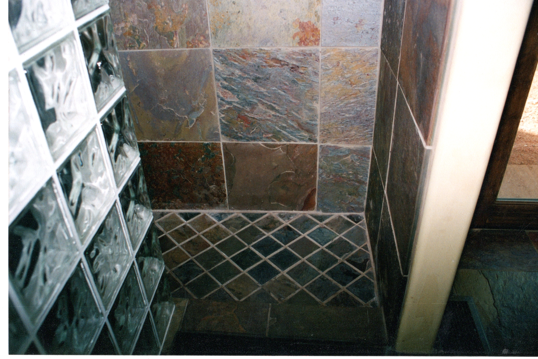 Shower tiled in slate with a diamond set pan and a glass block wall
