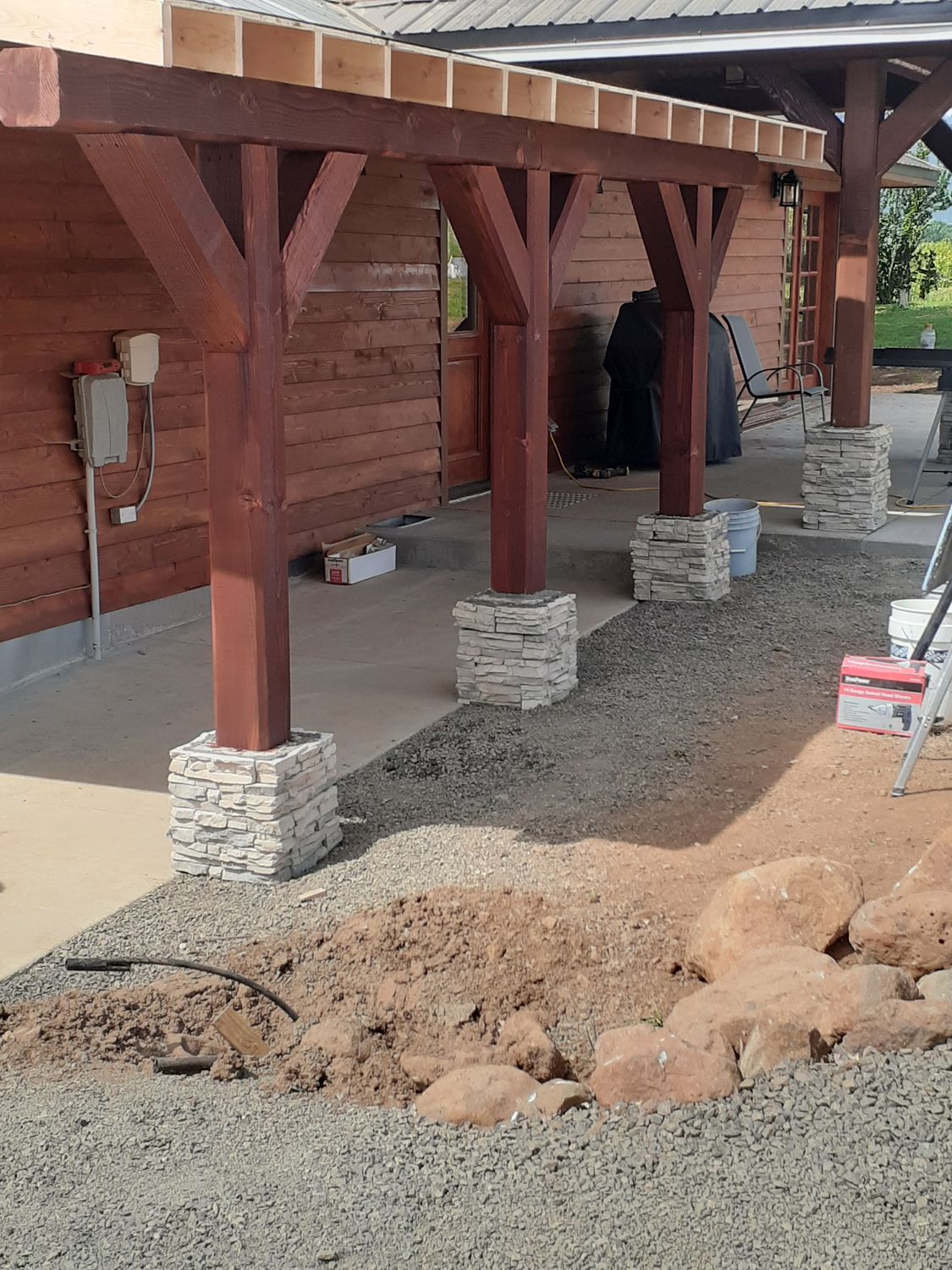 Covered porch under construction with stained timber posts set on cultured stone bases