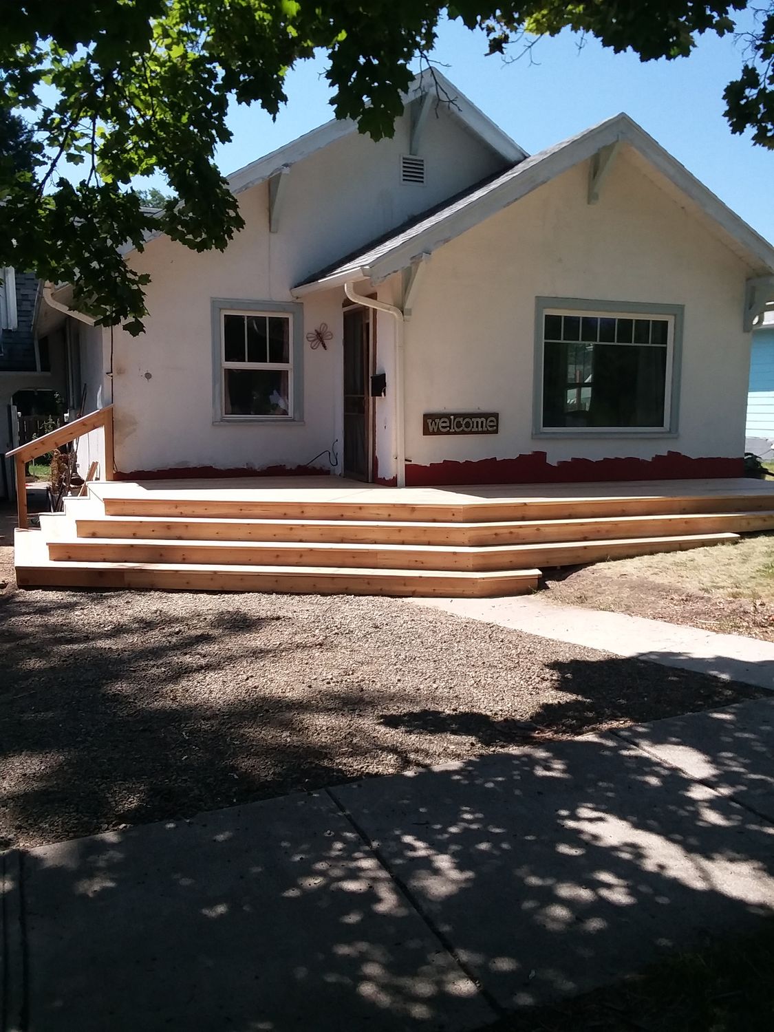 New cedar deck and wide entry steps across the front of a white bungalow